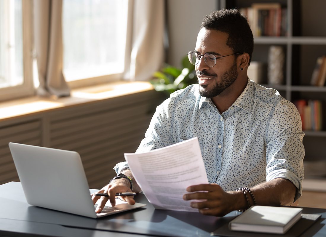 Blog - Happy Business Professional Sits at His Desk While Doing Research on a Laptop